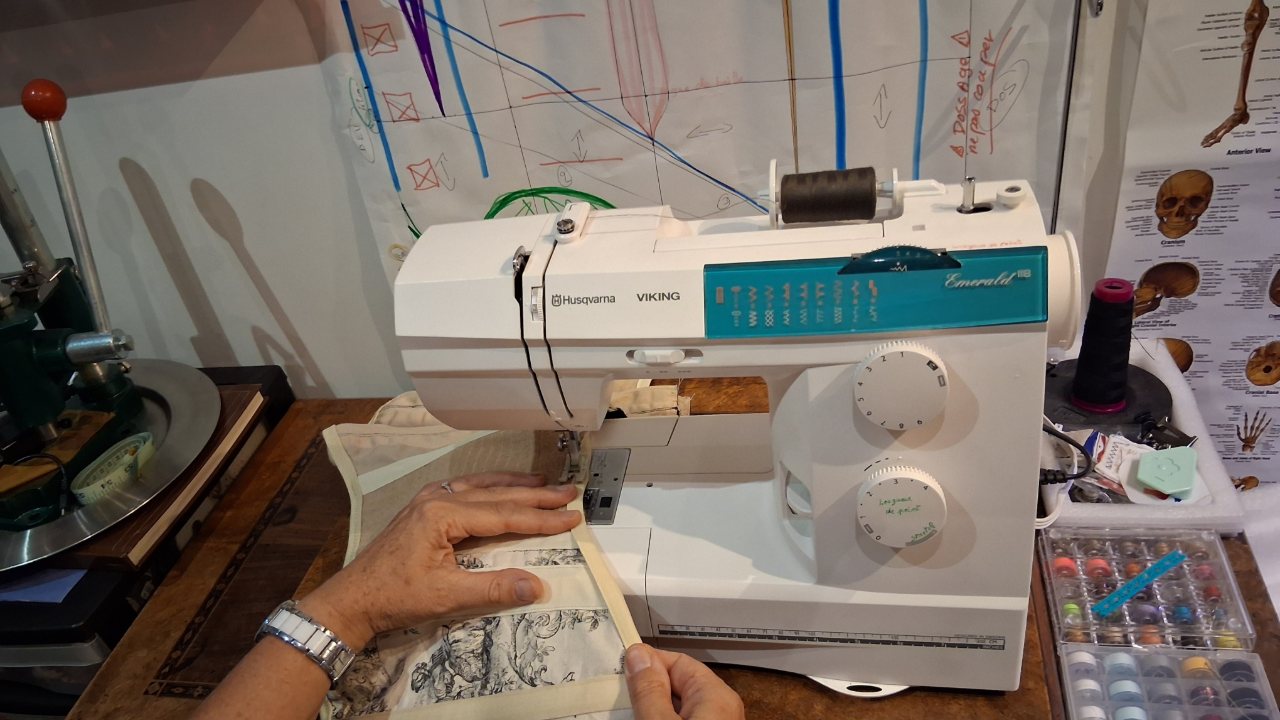 Les mains de la praticienne guident une ceinture lombaire en cours d'assemblage sous le pied de la machine à coudre.