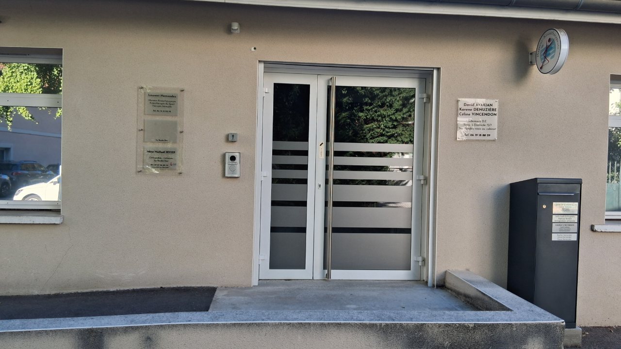 L'entrée du cabinet : une porte vitrée à deux battants, précédée d'une rampe, avec les plaques professionnelles de part et d'autre.