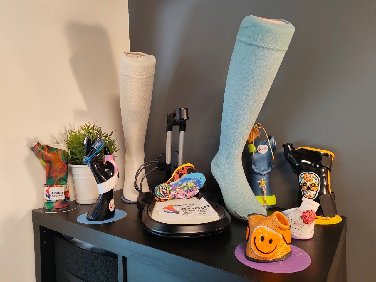 Une étagère du cabinet : des moulages de jambe, une main sculptée et des pièces orthopédiques colorées.