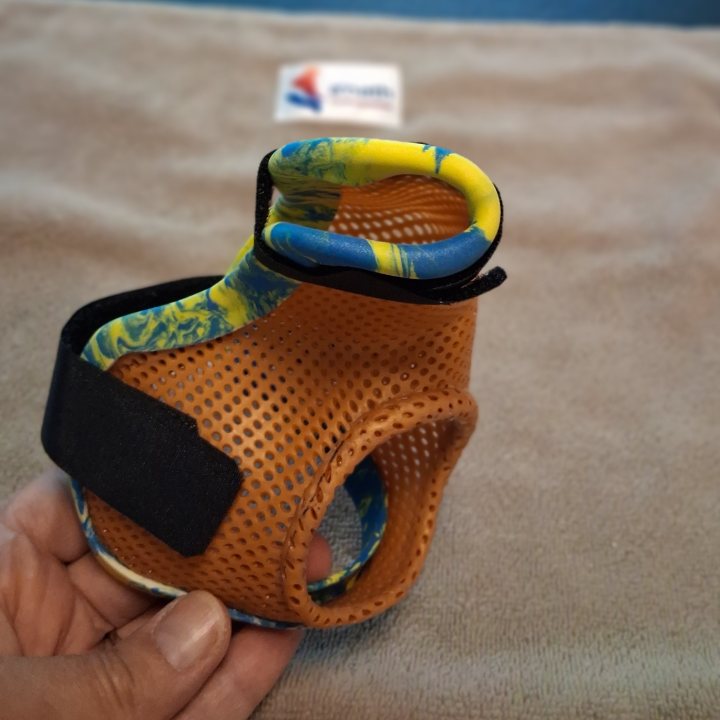 Une orthèse de main thermoformée, en thermoplastique orange perforé, avec sa sangle auto-agrippante, tenue en main après la découpe.
