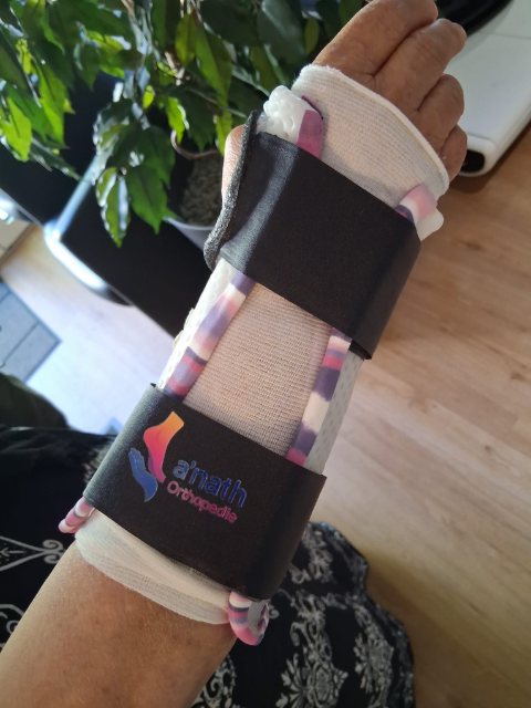 Orthèse de poignet thermoformée, bordée de rose, maintenue par deux sangles noires dont une porte le logo a'nath.