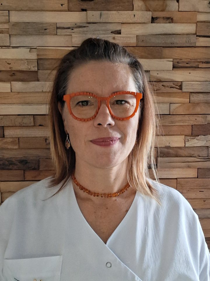 Nathaël Rivier, orthopédiste-orthésiste, en blouse blanche, devant un mur de bois.
