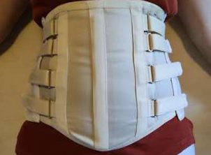 Ceinture lombaire sur mesure en toile blanche, serrée par des sangles latérales, portée à la taille.