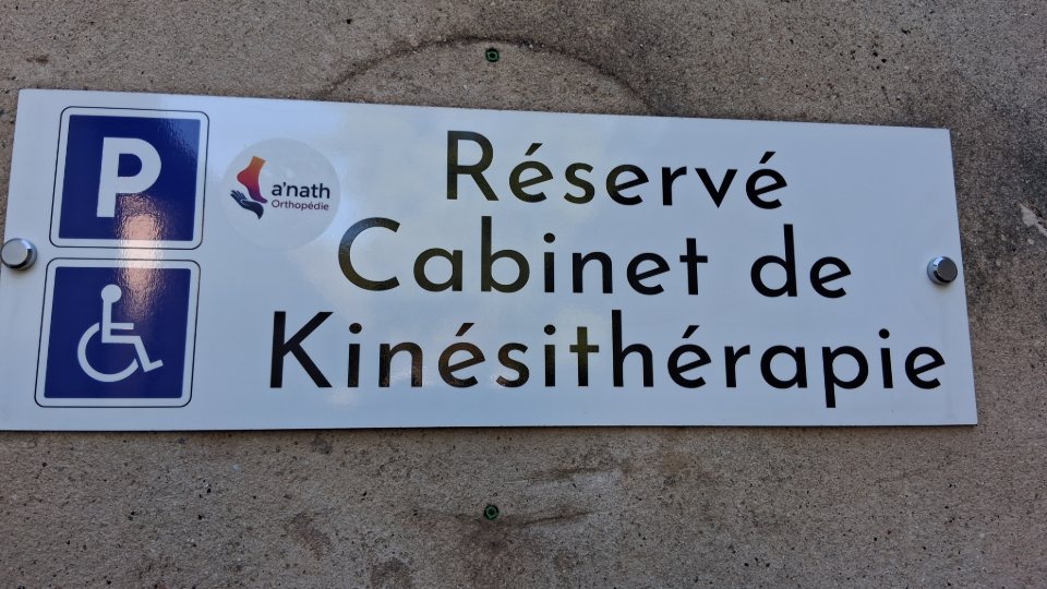 Le panneau de la place de stationnement réservée devant le cabinet, avec le pictogramme des personnes handicapées et le logo a'nath-Orthopédie.